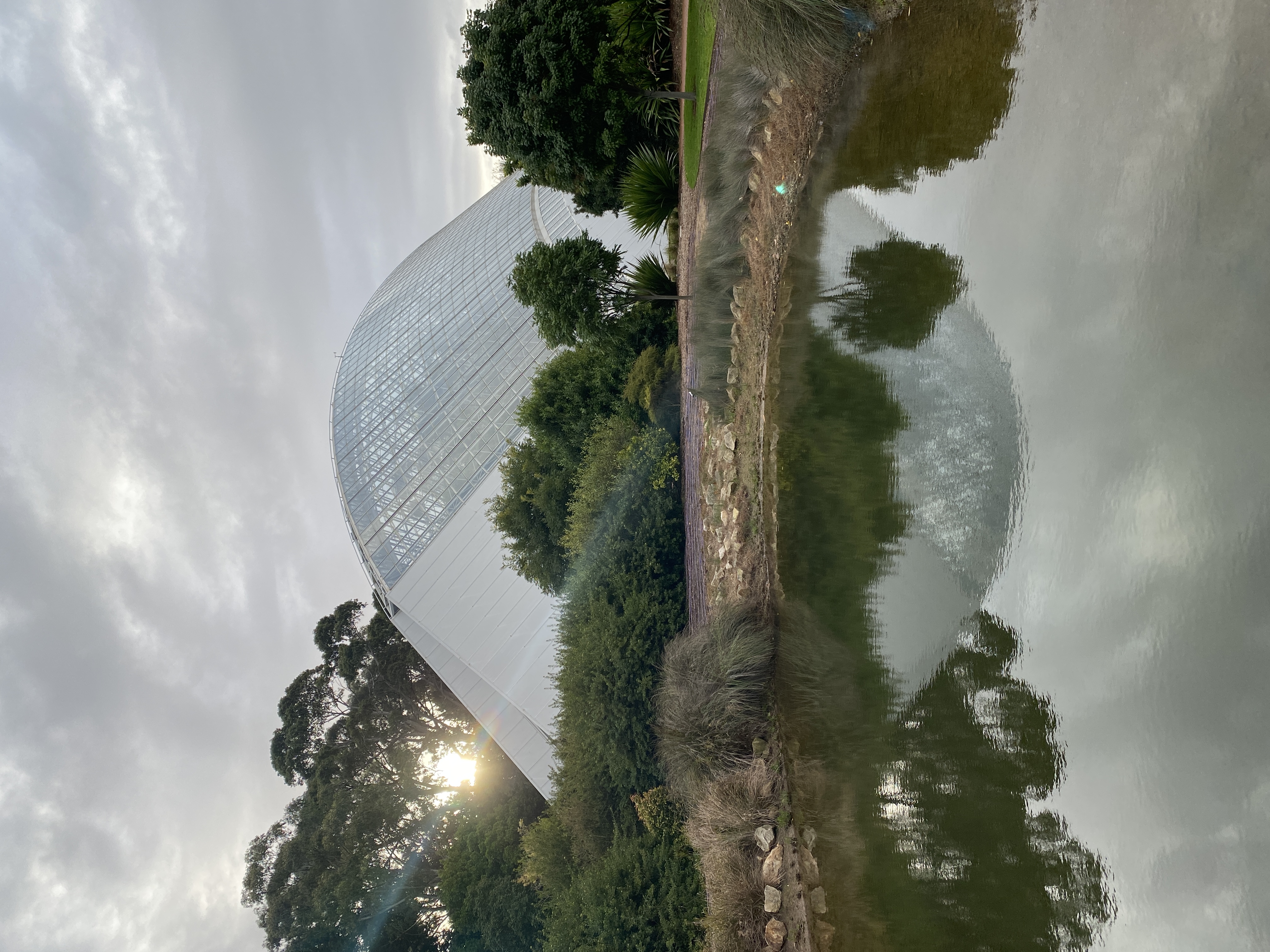 Bicentennial conservatory reflected in a lake in the setting sun