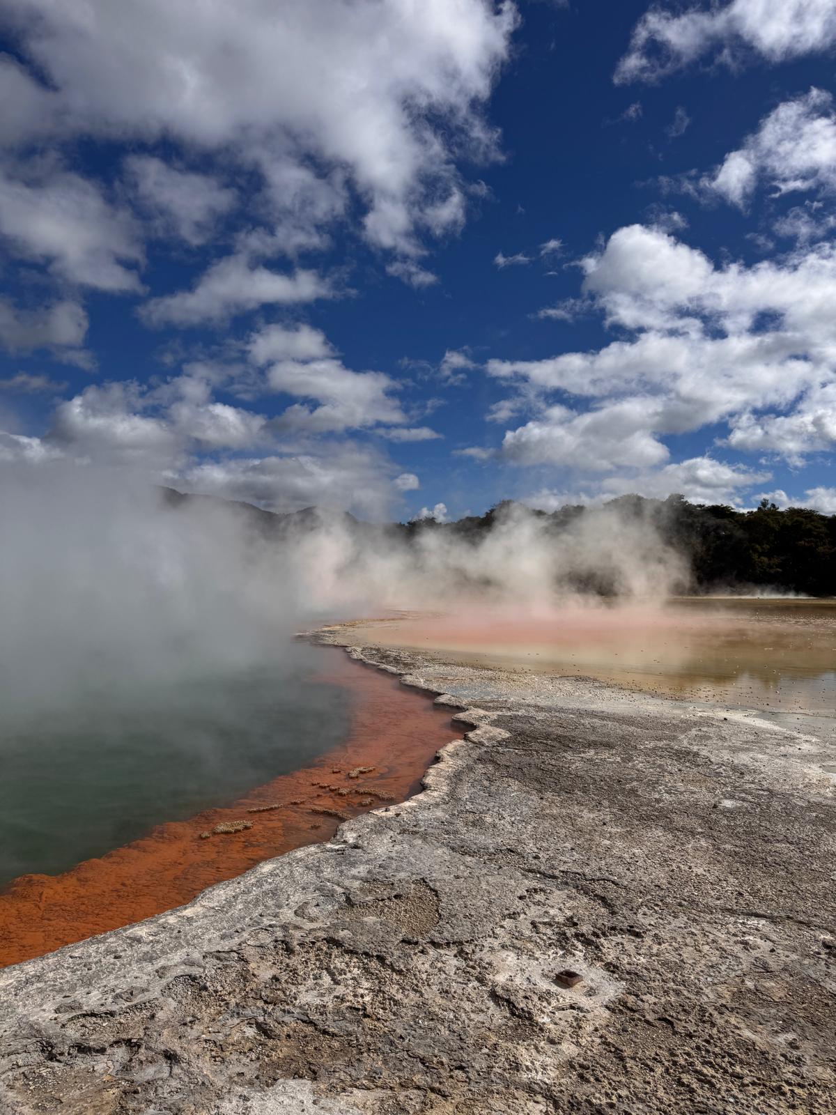 Steam rising from a geothermal pool beneath a cloudy sky